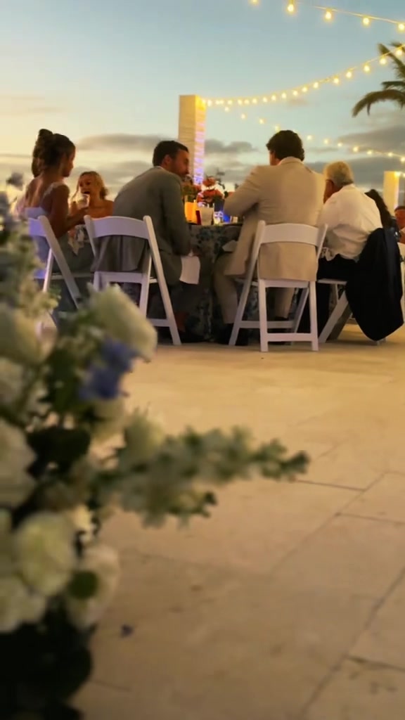 Wedding guests seated beneath string lights beside the Naples beach at sunset