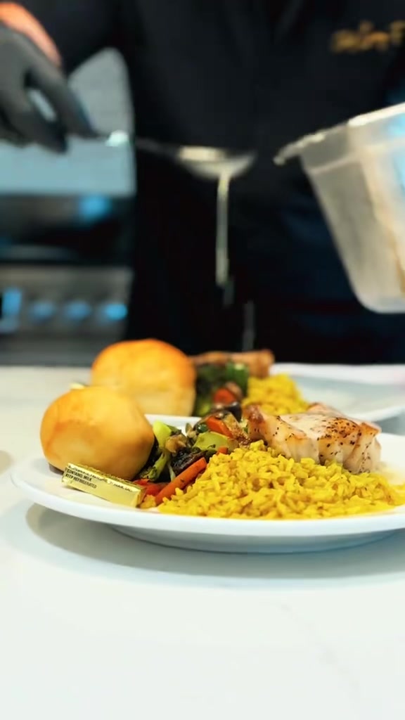 A chef finishes plated Gulf grouper with lemon butter, yellow rice, and roasted vegetables