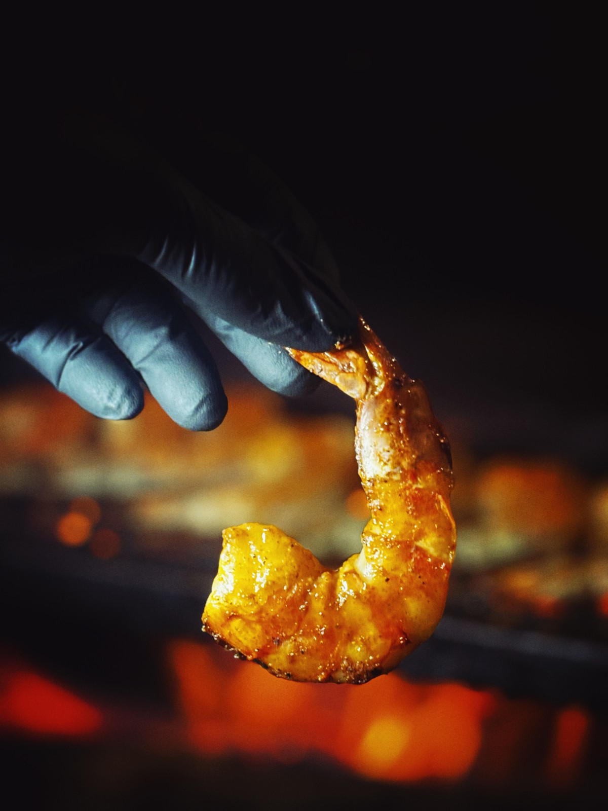 Close-up of grilled shrimp held above glowing coals