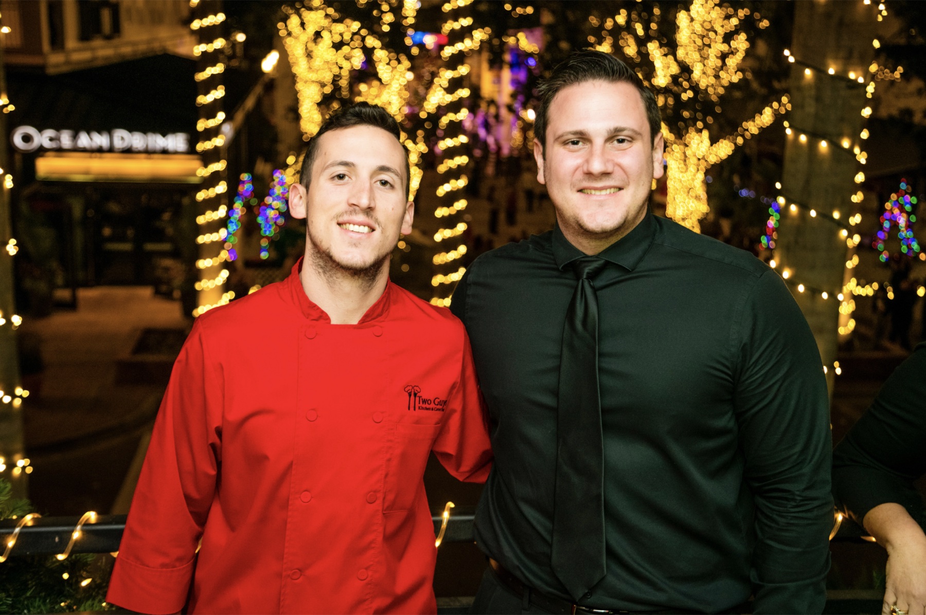 Two Guys team members together outdoors beneath holiday lights